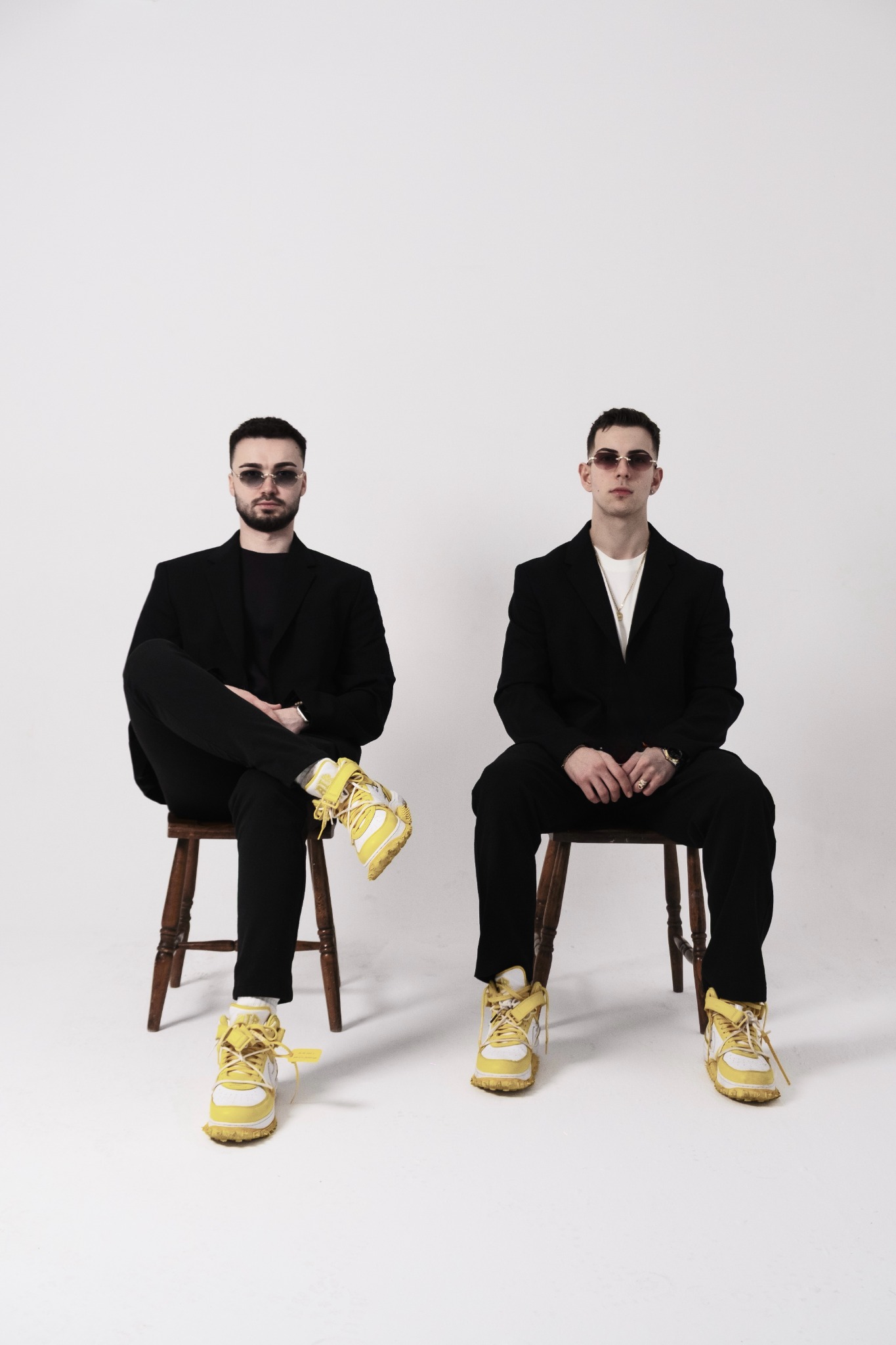 Seated portrait of 2side in black suits and yellow shoes